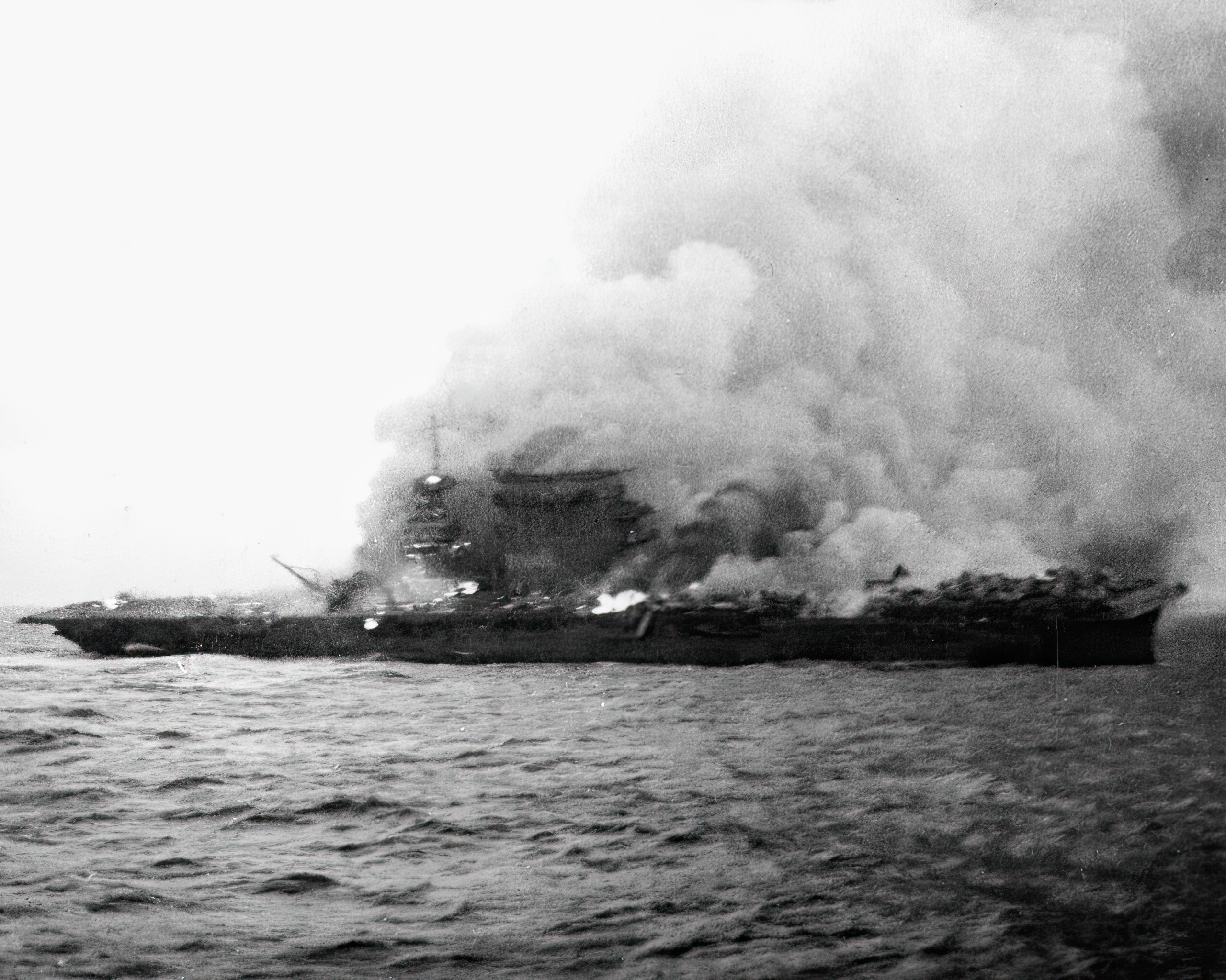 The U.S. Navy aircraft carrier USS Lexington (CV-2), burning and sinking after her crew abandoned ship during the Battle of the Coral Sea, 8 May 1942. Note the planes parked aft, where the fires have not yet reached